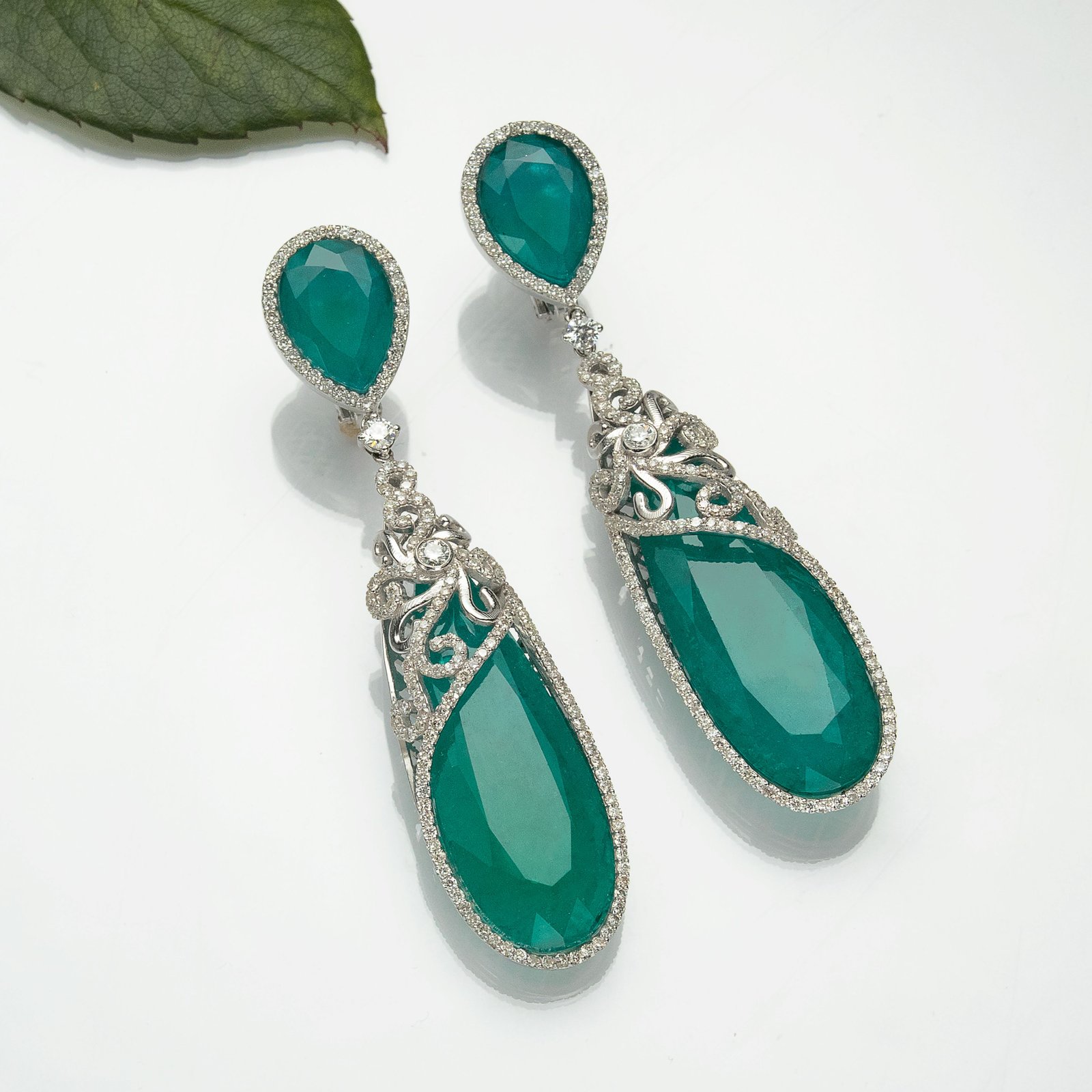 Long silver-tone drop earrings set with deep green pear-shaped stones in an ornate halo
