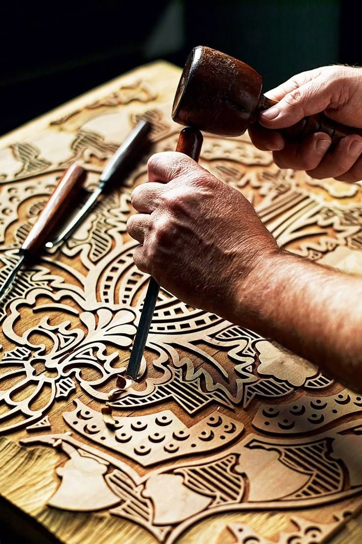 A mallet driving a chisel through a pierced ornamental wood panel