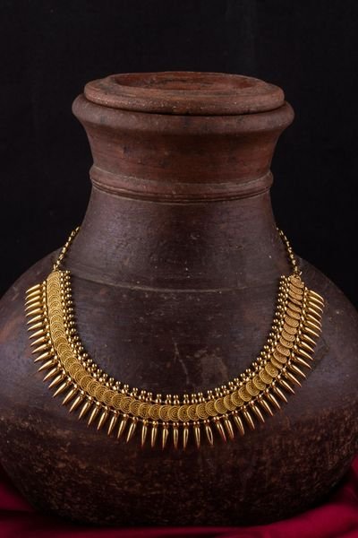 A traditional gold necklace and gold bangles arranged with a terracotta pot on red silk