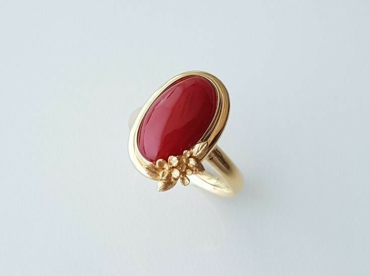 Ring with an oval cabochon red stone in a bezel setting with a floral accent