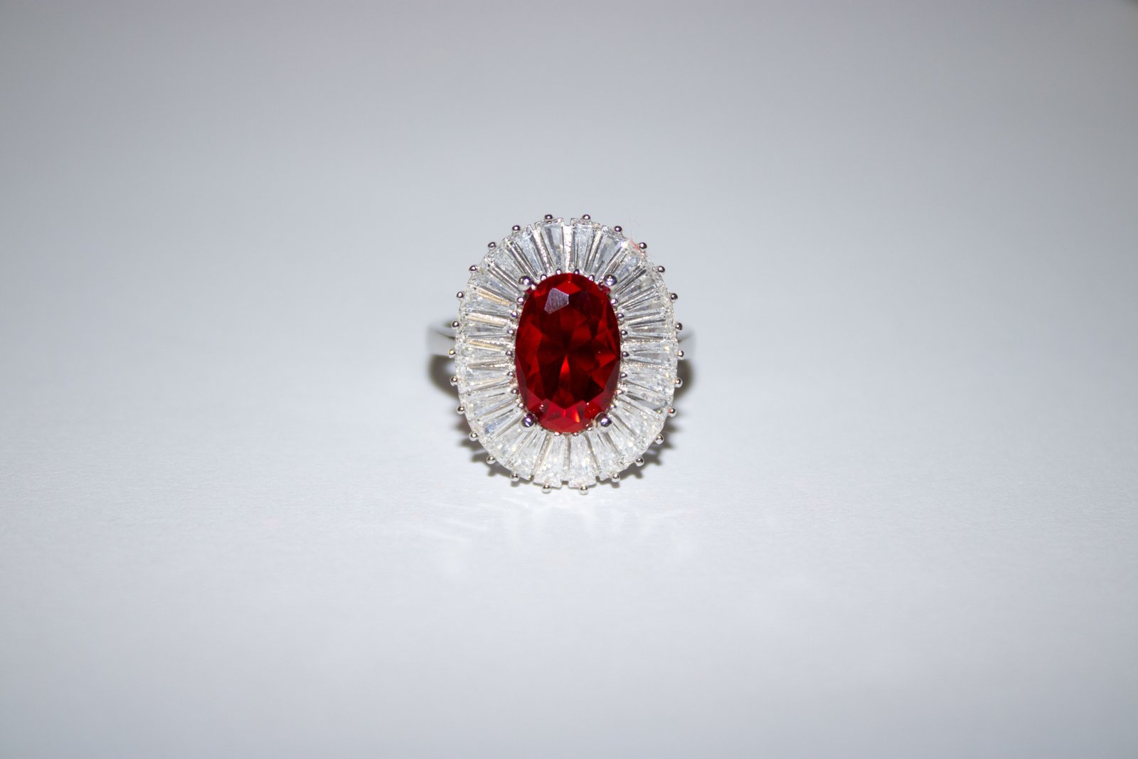 Ring with an oval red stone framed by a halo of tapered clear baguette stones