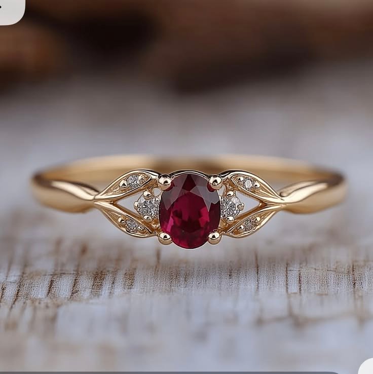 Ring with a red oval stone flanked by petal-shaped clusters of clear stones on a gold-toned band